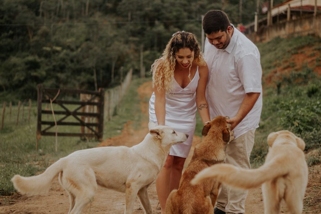 A couple in white outfits interacts with dogs on a rural path in Teófilo Otoni, capturing a joyful moment.